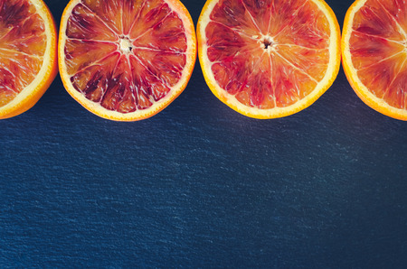 Raw of sliced blood oranges. Citrus background texture. Cut ripe juicy Sicilian Blood oganges fruits on back background. Minimalism style. Top view. Copy space.の写真素材