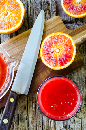 Preparation of Sicilian blood oranges juice on old wooden textured background. Freshly squeezed juice in a glass. Top view.の写真素材