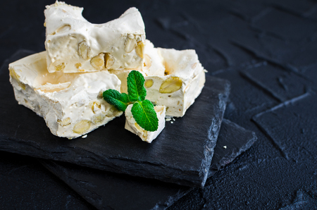 Delicious traditional Italian festive torrone or nougat with nuts on black stone background. Soft nougat blocks with almonds with fresh mint leaves. Holiday concept. Italian sweets.の写真素材