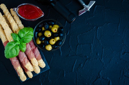 Bottle of wine with corkscrew and appetizers on dark stone background. Traditional wine tasting concept. Delicious antipasti on party or picnic time. Italian style banquet. Top view. Copy space.の写真素材