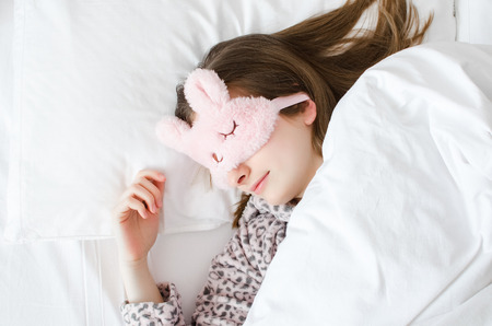 Beautiful young woman in cute sleep mask and warm pajamas lying down in the bed and sleeping in the...