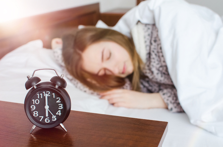 Young woman sleep with alarm clock near the bed in the morning. Sleeping girl and alarmclock in bedroom at home. Student or schoolgirl afraid to wake up late. Alarm clock anxiety. Oversleep concept.の写真素材