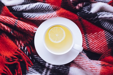 Cup of tea with lemon on red warm woolen blanket. Hot drink for rainy days. Hygge concept, autumn mood. Cozy winter morning at home. Warm and comfy fall weekend. Relaxing in cold weather. Top view.の写真素材