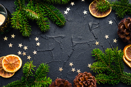 Christmas frame from fir tree branches with dried orange slices, pine cones and stars on black background with space for text. Merry Christmas and Happy New Year. Xmas concept. Top view. Copy space.の写真素材