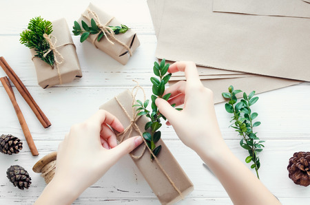 Process of wrapping modern Christmas presents with natural decorations on white background. Gifts boxes in craft paper with twine and green branches. Happy holidays concept. Top view. Flat lay.の写真素材