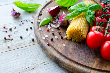 Ingredients for cooking Italian pasta - spaghetti, tomatoes, basil and garlic on wooden board on old rustic wooden table.の写真素材