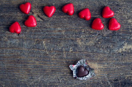 Valentines Day background with red chocolate heart shaped candies on a rustic wooden table with place for text.の写真素材