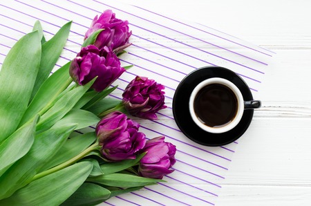 Cup of morning coffee and bouquet of spring flowers tulips over white wooden background. Top view. Morning greeting card. Holiday, romance of modern life concept. Close up.の写真素材
