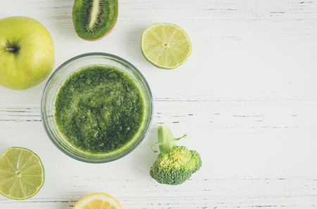 Green fruit and vegetable smoothie with ingredients: apple, kiwi, lemon, lime and broccoli on white wooden background. Spring detox concept. Clean eating. Healthy lifestyle. Top view. Copy space.の写真素材