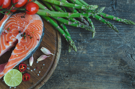 Frash raw salmon steak with vegetables and spices: asparagus, garlic, tomatoes, pepper corns, salt, chili and lemon on wooden cutting board. Healthy food diet concept. Top view. Copy space.の写真素材