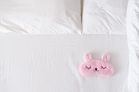 White bedding sheet, blanket and pillows with cute sleep mask on the bed. Rest, sleeping, comfort concept. Top view. Copy space.の写真素材