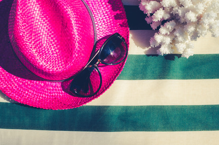 Colorful holiday background with pink straw beach hat with sunglasses and coral on striped sunbed. Summer vacation concept. Flat lay. Top view. Copy space.の写真素材