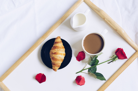 Romantic Valentines Day breakfast in bed, tray with fresh croissant, cup of coffee espresso with milk and red rose.の写真素材