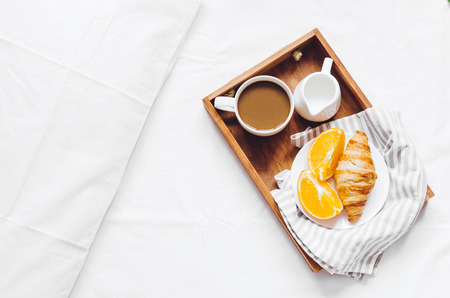 Romantic Valentines Day breakfast in bed, tray with fresh croissant, cup of coffee espresso with milk and fresh oranges.の写真素材