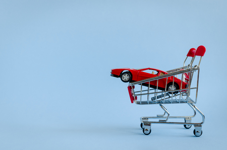 Car shopping concept. New red car in a shopping cart as a symbol for car buying and leasing. Blue background. Copy space.の写真素材
