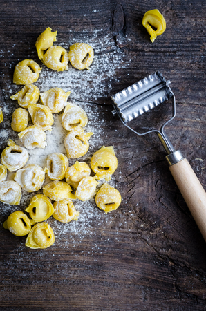 Freshly prepared homemade raw flouring tortellini ready to cook on wooden vintage cutting board. Traditional Italian cuisine concept. Top view.の写真素材