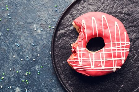 Pink frosted donut with bite missing on dark background. Top view. Copy space.