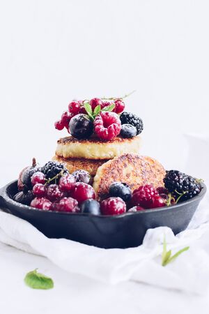 Cottage cheese pancakes served with lots of fresh berries on white background. Gourmet Breakfast - Cottage cheese syrniki, curd fritters with raspberry, strawberry, blueberry. Close up. Copy space.の写真素材