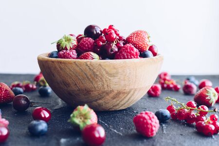 Bowl of various summer organic berries. Large collection of freshly picked ripe berries on black background. Agriculture, gardening, harvest concept.の写真素材
