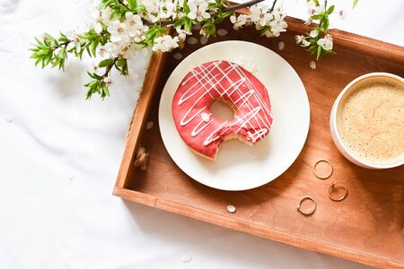 Spring breakfast in bed. Tray with strawberry pink donut with coffee and spring blossom. Girl...
