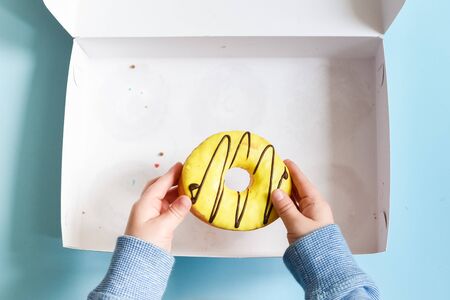 Donut box with a young male child's hand reaching to grab the last yellow banana frosted doughnut...