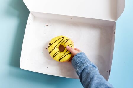 Donut box with a young male child's hand reaching to grab the last yellow banana frosted doughnut...