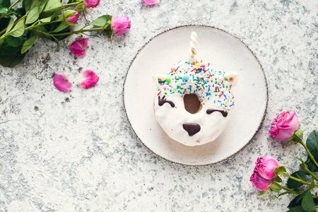 Unicorn donut with pink roses over light background. Trendy doughnut unicorn with white glaze. Valentine's day greeting card. Mothers Day concept. Mother's gift. Top view. Copy space.の写真素材