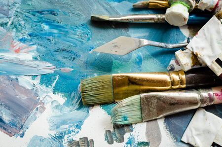 Artist paint brushes and oil paint tubes on wooden palette. Texture mixed oil paints in different colors. Instruments and tools for creative leisure. Painting hobby. Top view. Copy space.の写真素材
