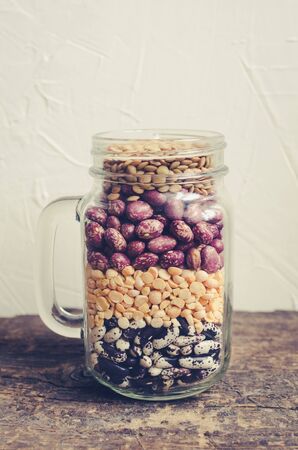 Assortment of dry organic beans and lentils layered in glass jar on old rustic wooden table. Variety of raw legumes. Balanced diet, cooking, vegetarian and clean eating concept. Healthy food.の写真素材