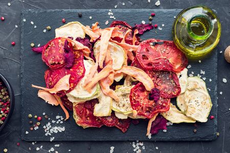 Healthy homemade vegetable chips from beetroot, tomatoes, carrot and zucchini on black background. Organic diet food. The vegan diet. Dried vegetables. Vegetarian snack concept. Top view. Copy space.の写真素材