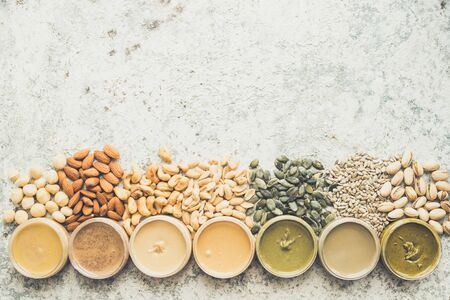 Nuts and seeds butter in jars with ingredients. Homemade raw organic peanut, almond, hazlenut, cashew, pistachio, macadamia nuts paste and sunflower and pumpkin seeds butter. Top view. Copy space.の写真素材