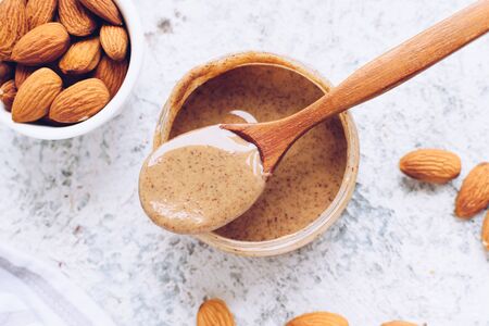 Almond nut butter in glass jar. Homemade raw organic almond nuts paste on greyの写真素材