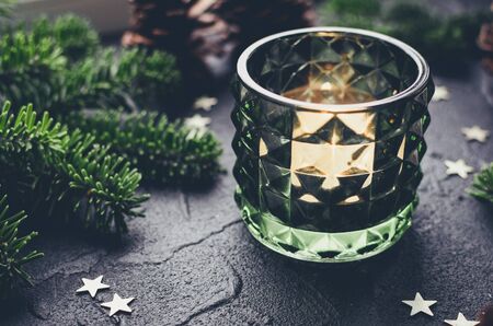 Christmas still life with lighted candle, fir tree branches, pine cones and stars on darkの写真素材