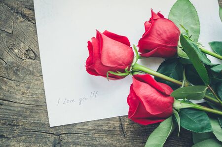 Red roses flowers on old wooden background with text I love you. Romantic Valentines holidays...