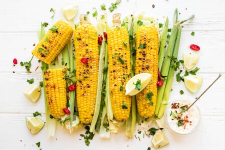 Grilled corn cobs in mexican style with lime, cilantro, chili and sauce on white wooden