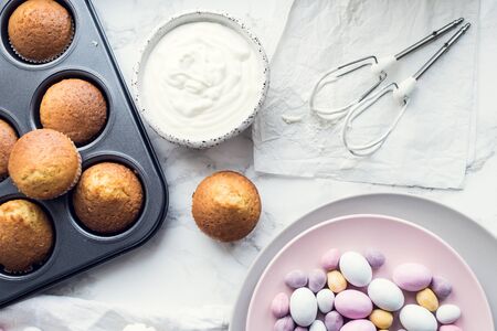 Process of preparation glazed Easter cupcakes decorated with mini chocolate eggs candy on white...
