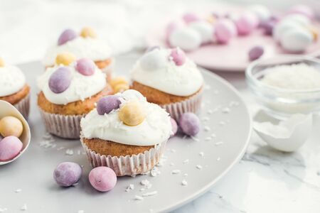 Glazed Easter cupcakes decorated with mini chocolate eggs candy on white marble background. Happy...