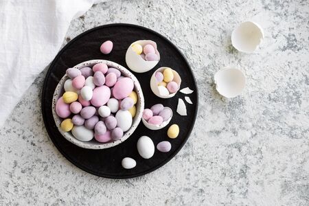 Easter composition with mini chocolate eggs in pastel colors on grey concrete background. Happy...