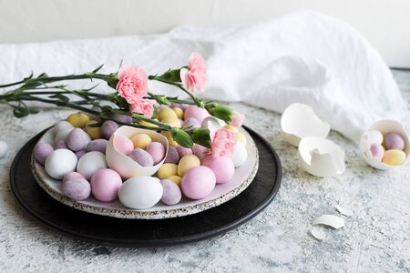 Easter composition with mini chocolate eggs in pastel colors and pink flowers on grey concrete...