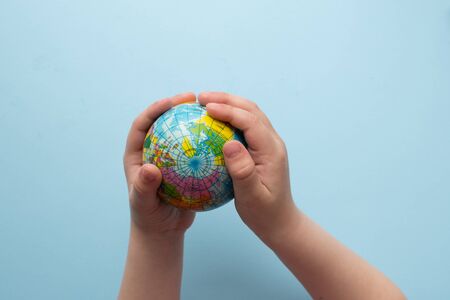 Child holds small globe in hands on blue background. Earth day. Green concept. Studies of geography. Self education. Close up. Top view. Copy space.の写真素材