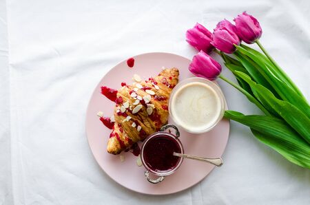 Cup of coffee with foam and bouquet of pink tulips on white bed honeymoon.