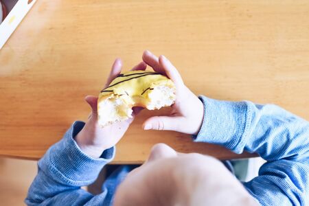 Little boy is eating yellow banana frosted donut.