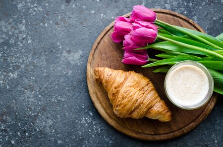 Cup of coffee with bouquet of pink tulips and croissant on blackの写真素材