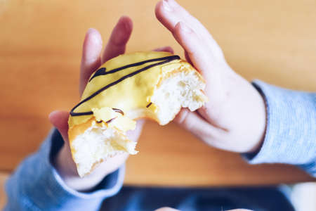 Little boy is eating yellow banana frosted donut. Tasty food for kids. Family eating donuts from...