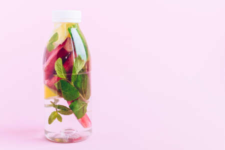 Bottle of detox water with rhubarb, mint and lemon on pink background. Rhubarb lemonade. Fresh...