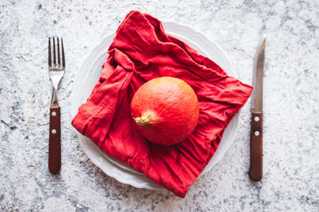 Thanksgiving autumn place setting with cutlery and arrangement of fall leaves and pumpkin on grey...