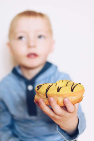 Little boy is eating yellow banana frosted donut. Tasty food for kids. Family eating donuts from food delivery. Unhealthy lifestyle concept.の写真素材