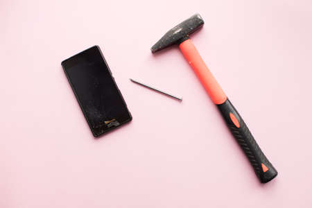 Hammer, nail and mobile phone with broken display on pink background. Crashed smartphone concept. Top view.の写真素材