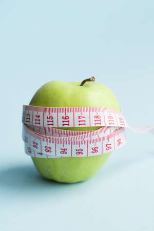 Apple with measuring tape on blue background. Weight loss, counting calories and healthy eating...