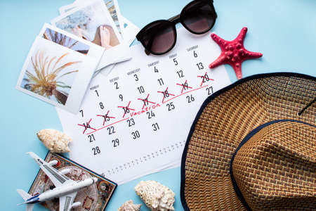Vacation planning concept. Travel preparation: camera, passport, vacation plan written on calendar and sunglasses on blue background. Flat lay. Top view.の写真素材